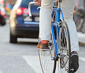 Hombre montado en bicicleta circulando por la calle de una ciudad con coches